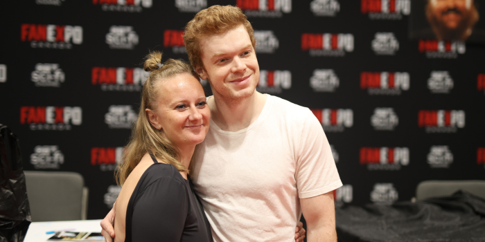 Cameron Monaghan poses with a fan, both smile at the camera as they stand in close for the photo.