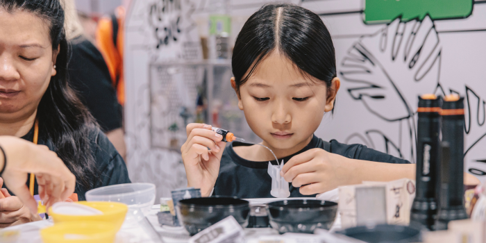 A mother and daughter build miniatures at the Miniverse booth. The child is using liquid to fill a mould.