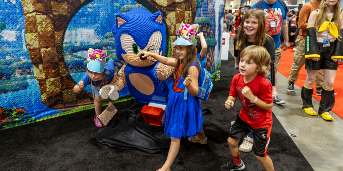 Four kids, posed as if they're running, stand beside a life-sized Sonic the Hedgehog made of Lego.
