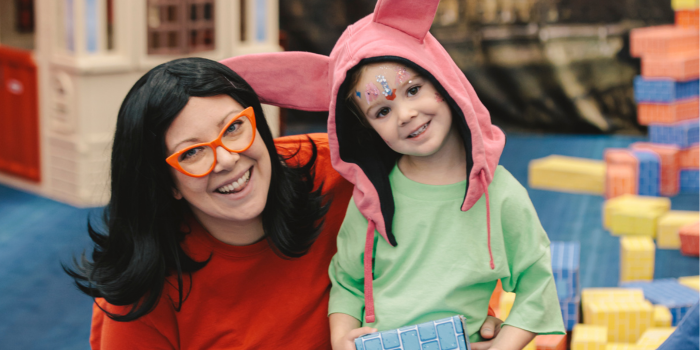 A mother and child pose in the Kids' Zone, the child holds a cardboard coloured brick. They smile at the camera and are dressed as Linda and Louise Belcher respectively. 