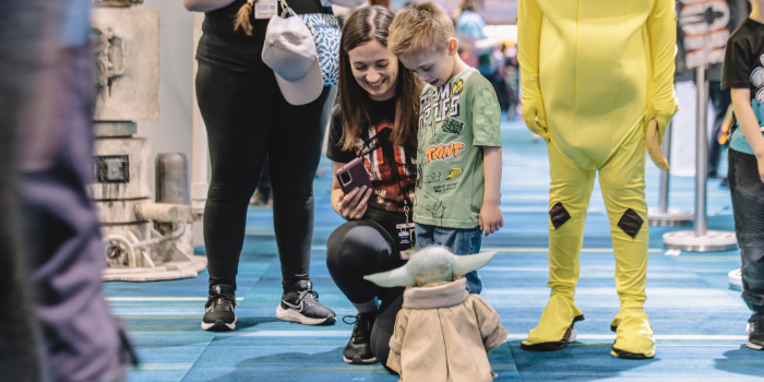A mother and son greet a small animatronic Grogu that's rolling toward them. They smile at the small green creature as it approaches.