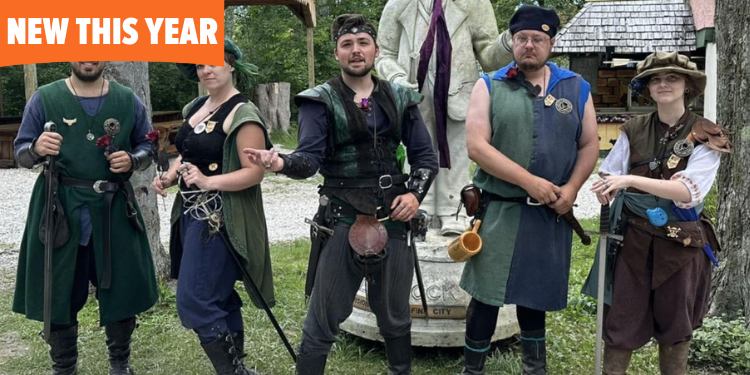 Five people dressed in medieval-inspired outfits pose outdoors near a statue, wearing leather armor, tunics, and accessories like swords and drinking horns. They stand confidently, ready for adventure.