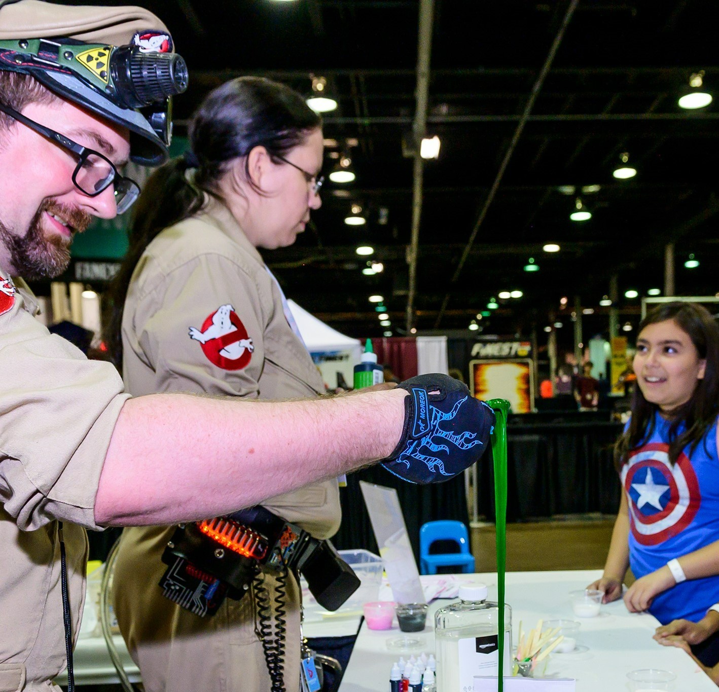 Two ghost busters lifting up green slime in front of children. One girl is wearing a Captain America shirt and is looking at it in awe.