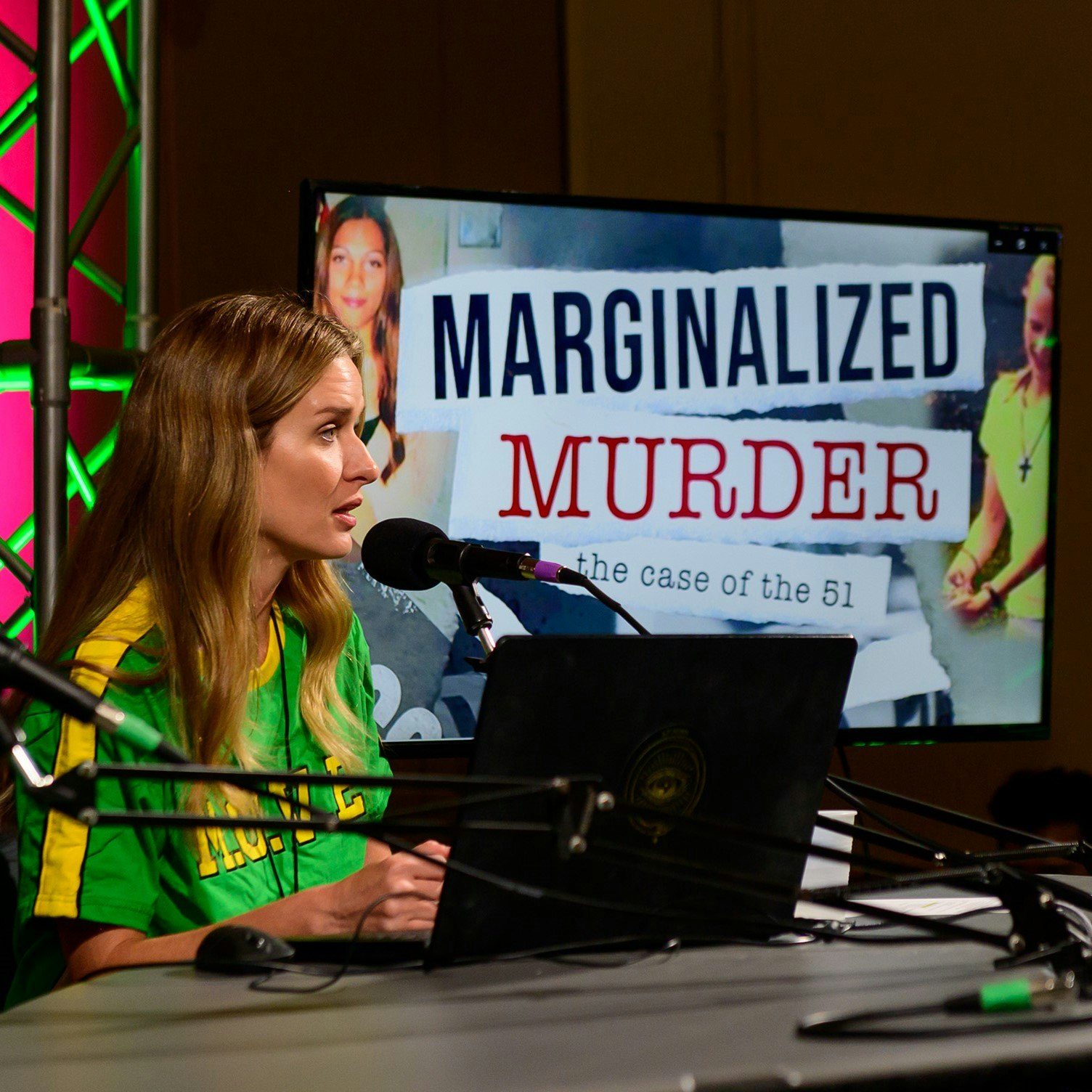 Image of Carly Roland, wearing a green and yellow jersey, talking into a mic with a computer in front of her. In the background on a screen is the image of "Marginalized Murder: the case of the 51".