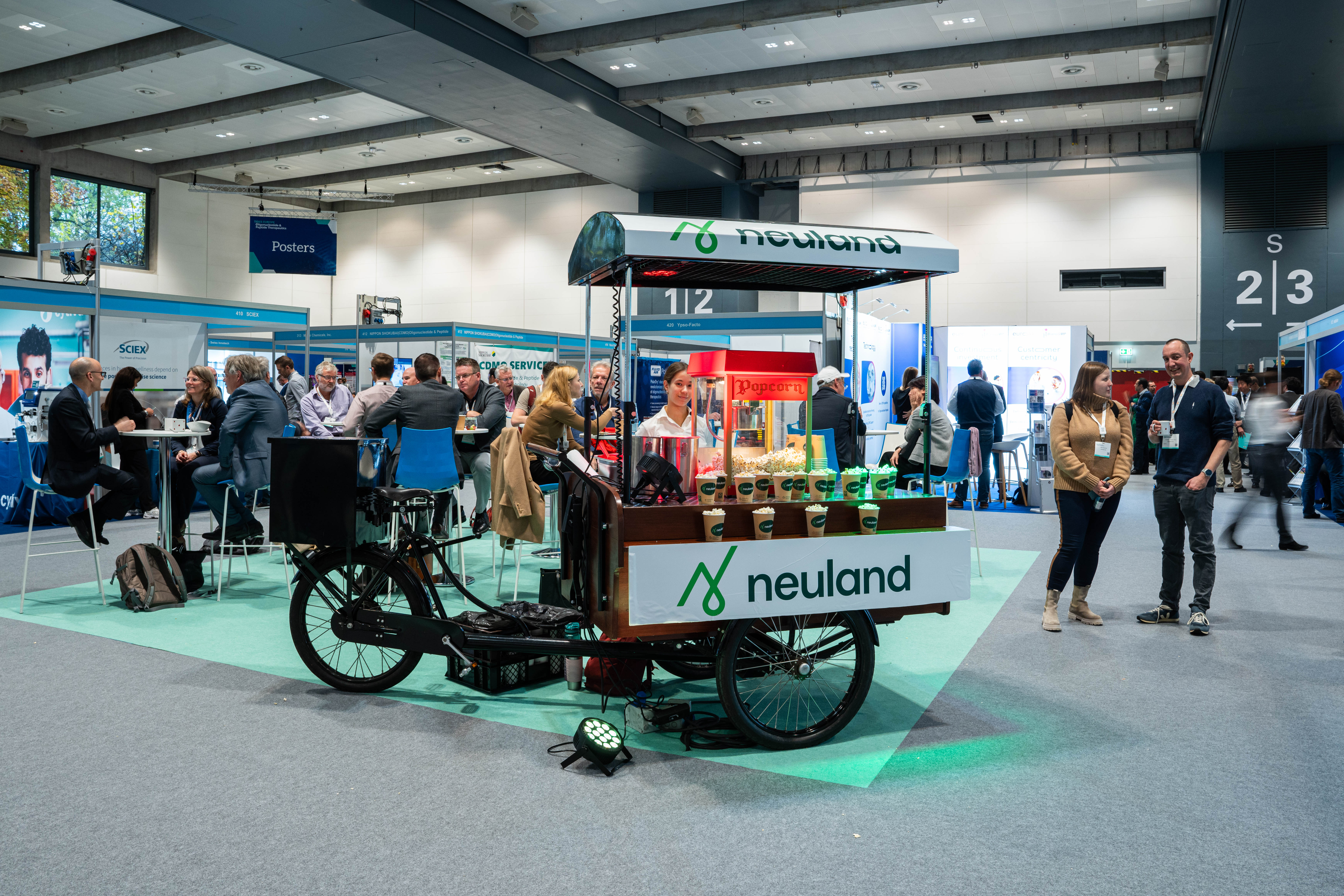 Neuland branded coffee stand sitting on bicycle wheels in the exhibit hall.