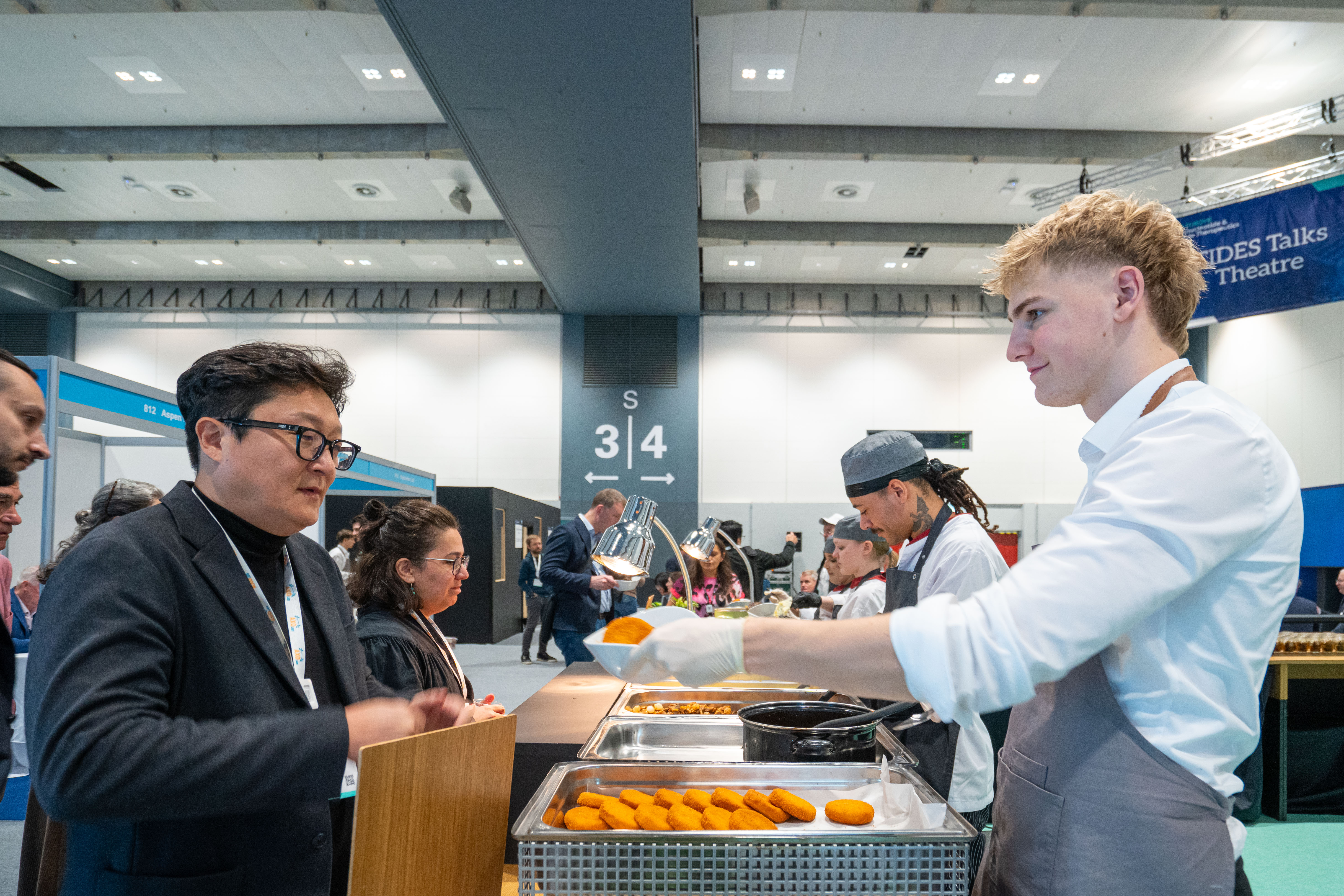 A man in a black suit collects food from staff in the exhibit hall.