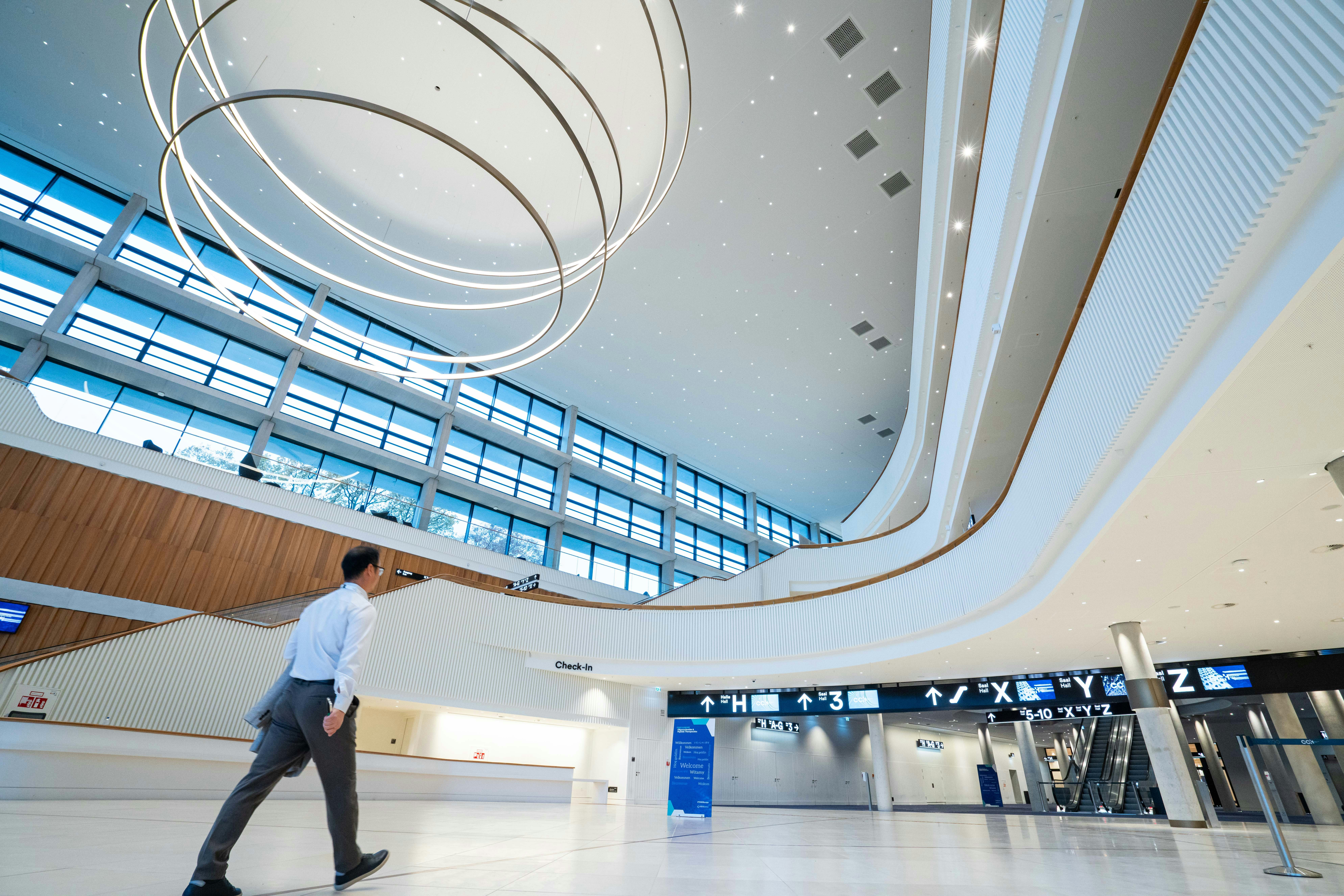 Inside the Hamburg Congress Center with white modern interior design, a man walking past and a large, circular ceiling light