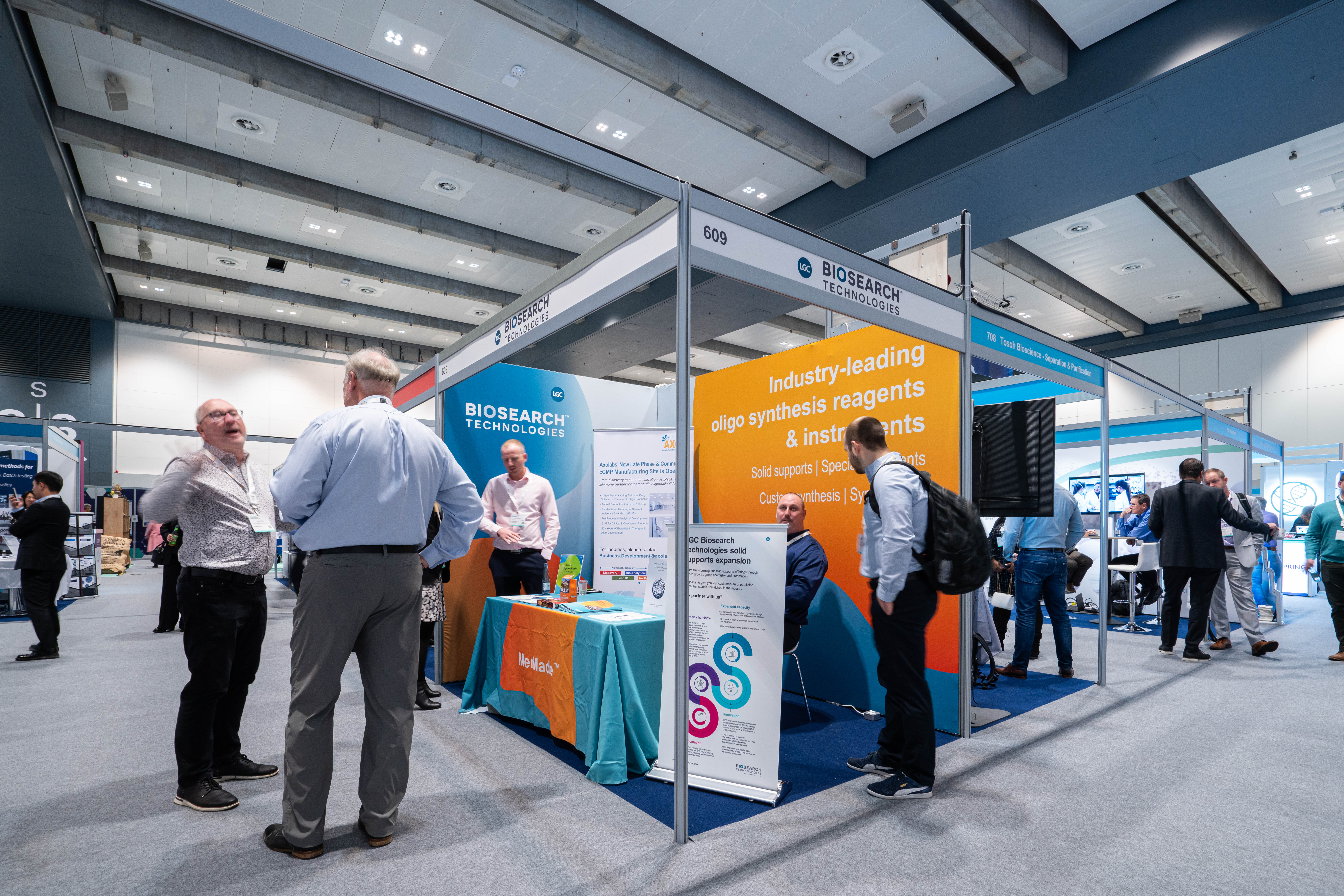 Two men are in deep conversation as another attendee speaks to an exhibitor at TIDES Europe.