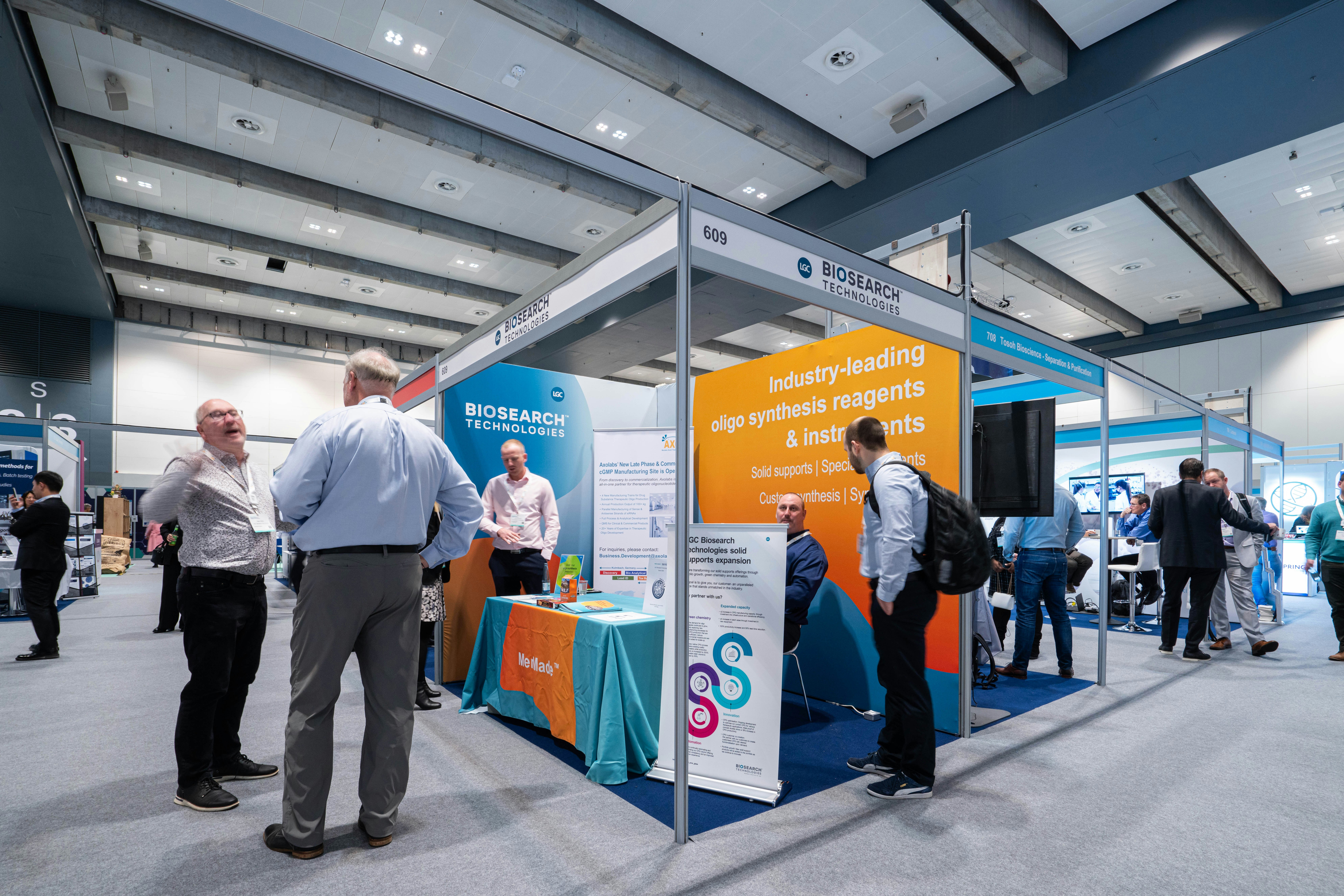 Two men are in deep conversation as another attendee speaks to an exhibitor at TIDES Europe.