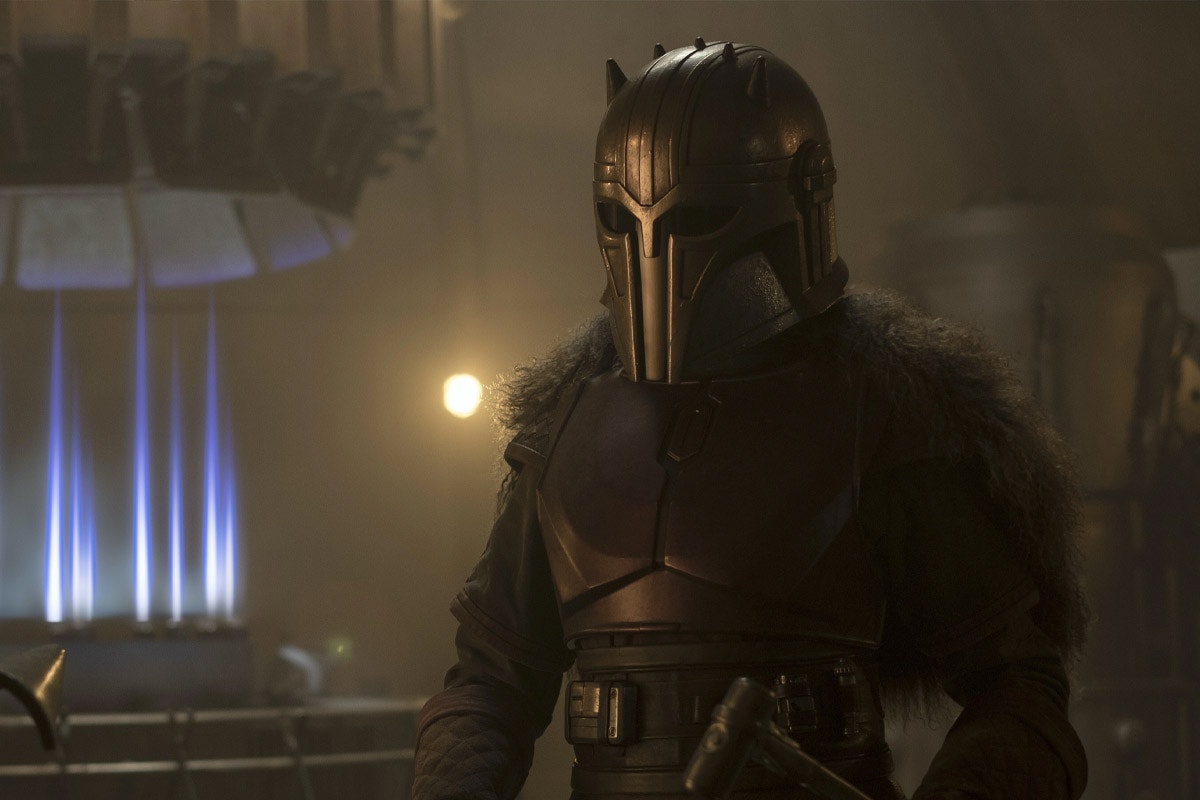 The Armorer stands near open flames while fully masked