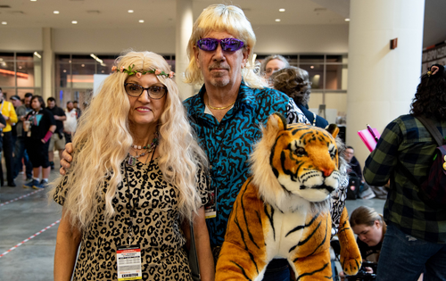 two cosplayers dressed as Carol Baskin and Joe Exotic from Tiger King, holding a stuffed animal tiger