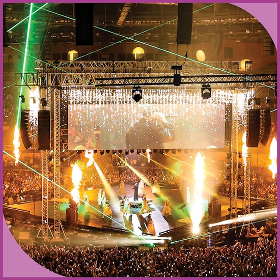 Concert on a square stage with a large screen and numerous effects, including fire.