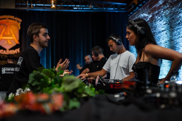 DJ instructor teaching a group of adults at Tomorrowland Academy, with participants using headphones and DJ consoles during a hands-on session.