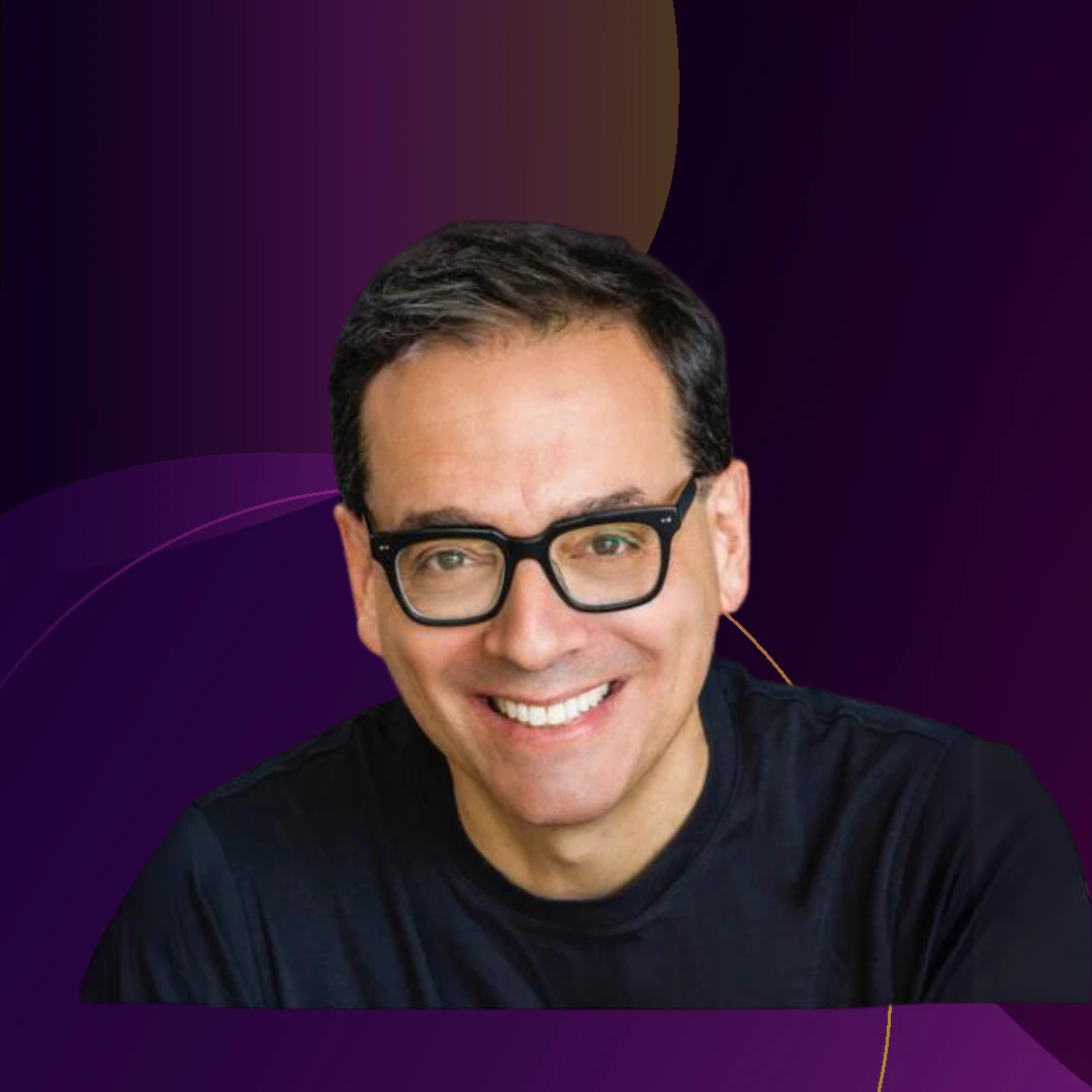 Portrait of Daniel Pink with glasses, smiling against a dark purple background