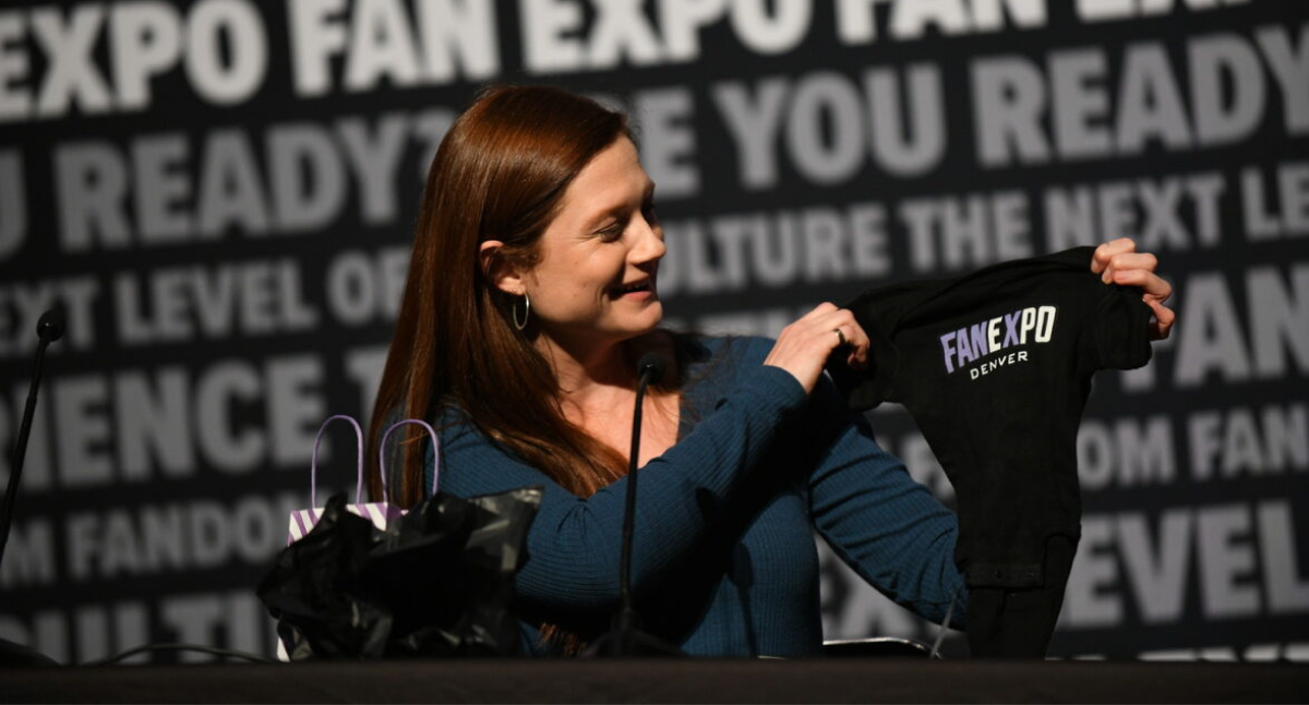 Bonnie Wright smiles as she opens her custom FAN EXPO Denver baby onesie