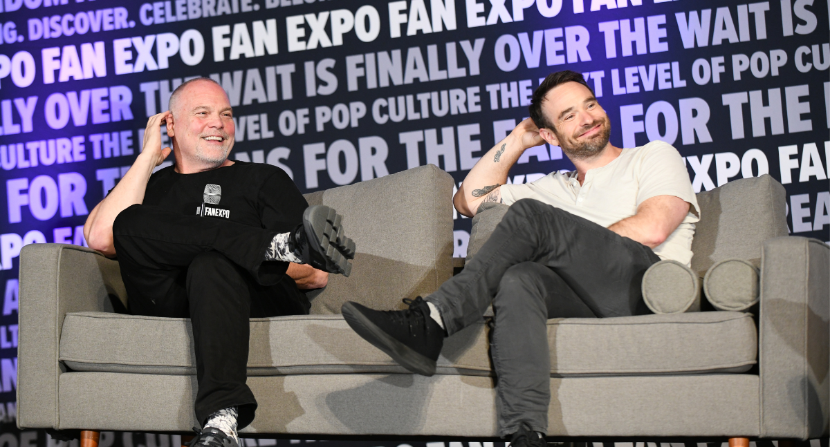 Crosslegged, Vincent D'Onofrio and Charlie Cox sit, smiling, and looking toward the moderator. They are on a grey-beige couch.