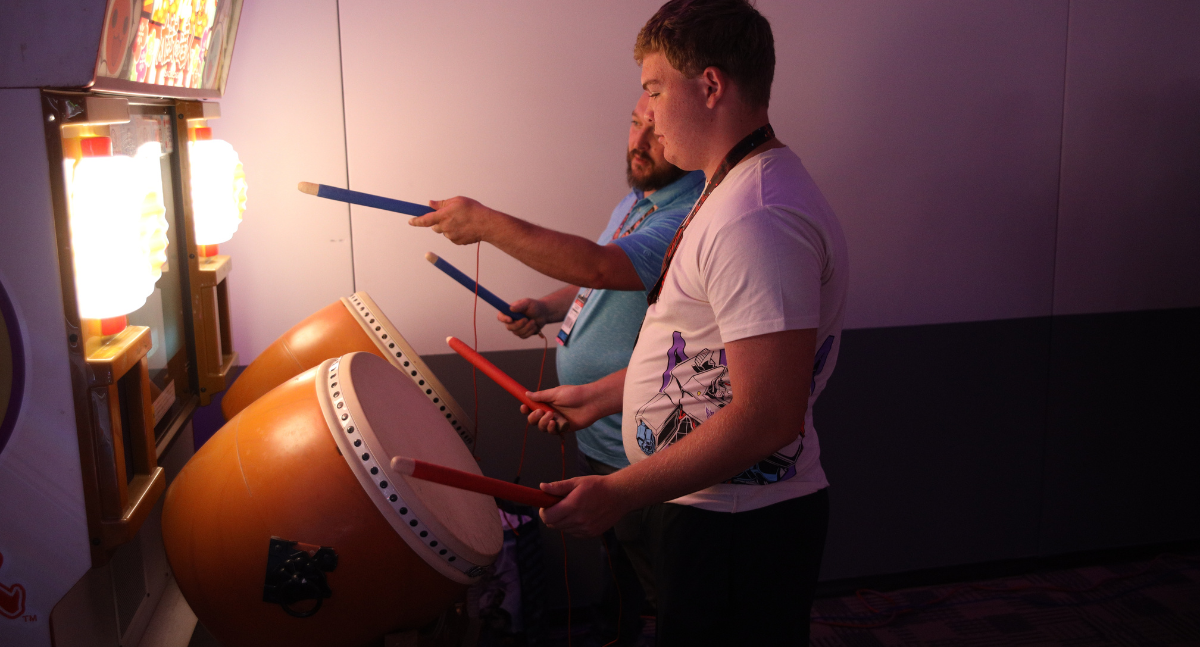 Fans play the drumming game in the japanese arcade. The light from the machine illuminates their faces.