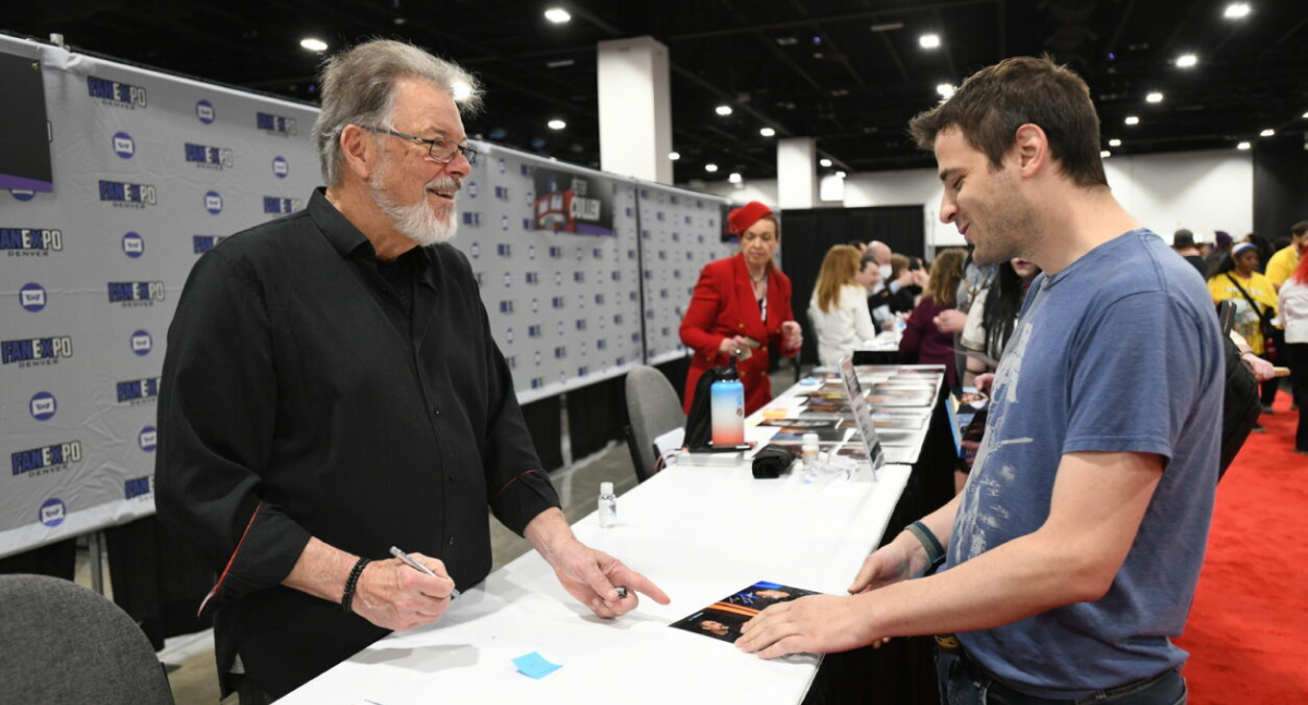 Jonathan Frakes and a fan share a smile as he hands back his signed picture