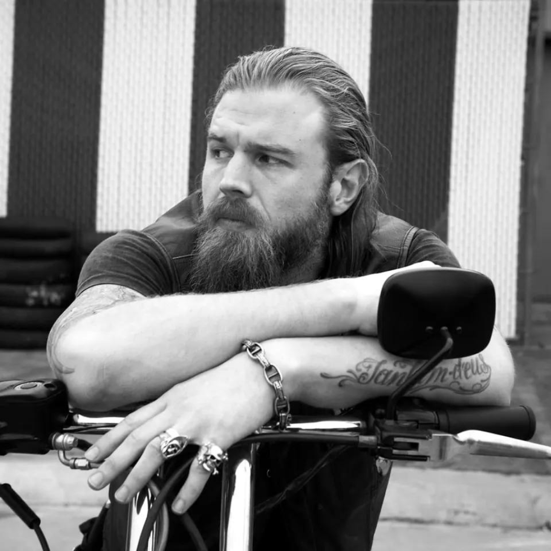 Black and white photo of Ryan Hurst as Opie on bike from Sons of Anarchy. He is leaning on the handles and looking to the left.