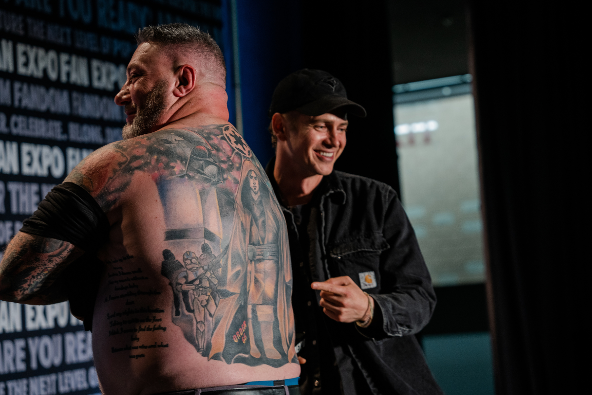 Hayden Christensen standing next to a guy pointing at the guy's Order 66 tattoo on his back