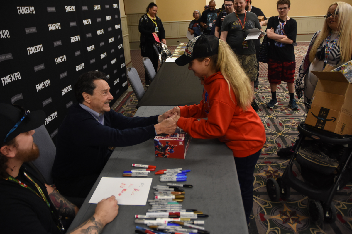 Peter Cullen at his table holding a young girls hand and they are smiling