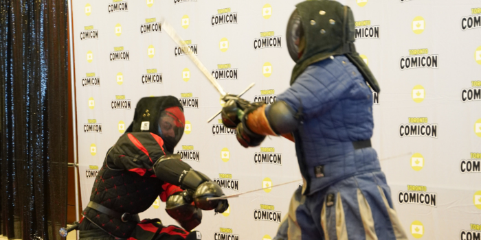 The Oxford Ren Festival knights hit the cosplay red carpet for the Great Toronto Comicon Knight Fight. It's the red and black knight against the blue and grey. the Red and black clothed knight is swinging low, while blue and grey swings high.