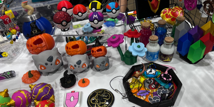 a table full of products, including 3D printed pokeballs, potions, and Bulbasaurs with pumpkins on their backs