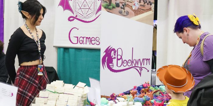 Artist watches two shoppers as they admire dragon and animal figures at event booth.