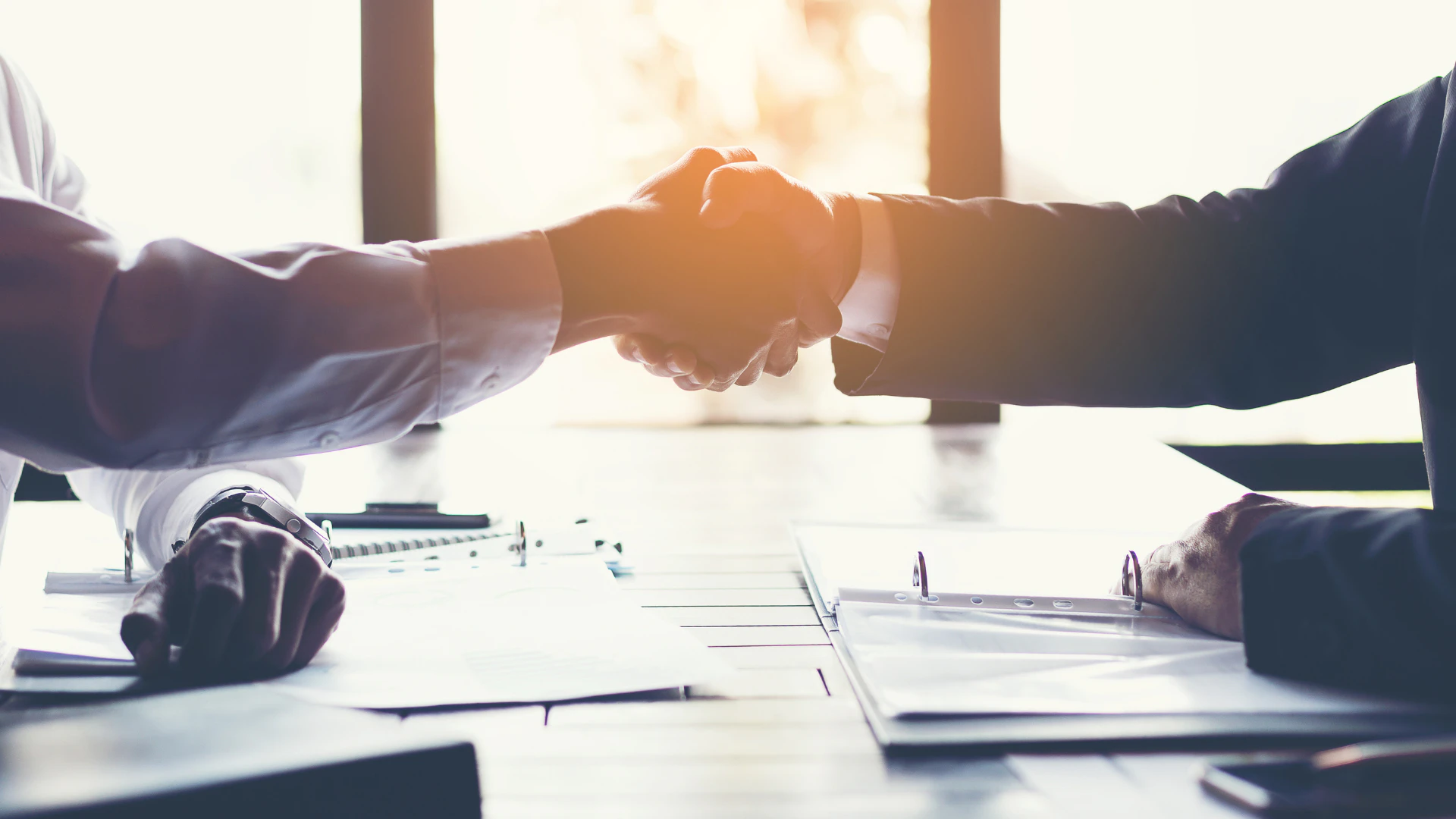 Two energy sector professionals shaking hands over signed contract documents at a negotiation table