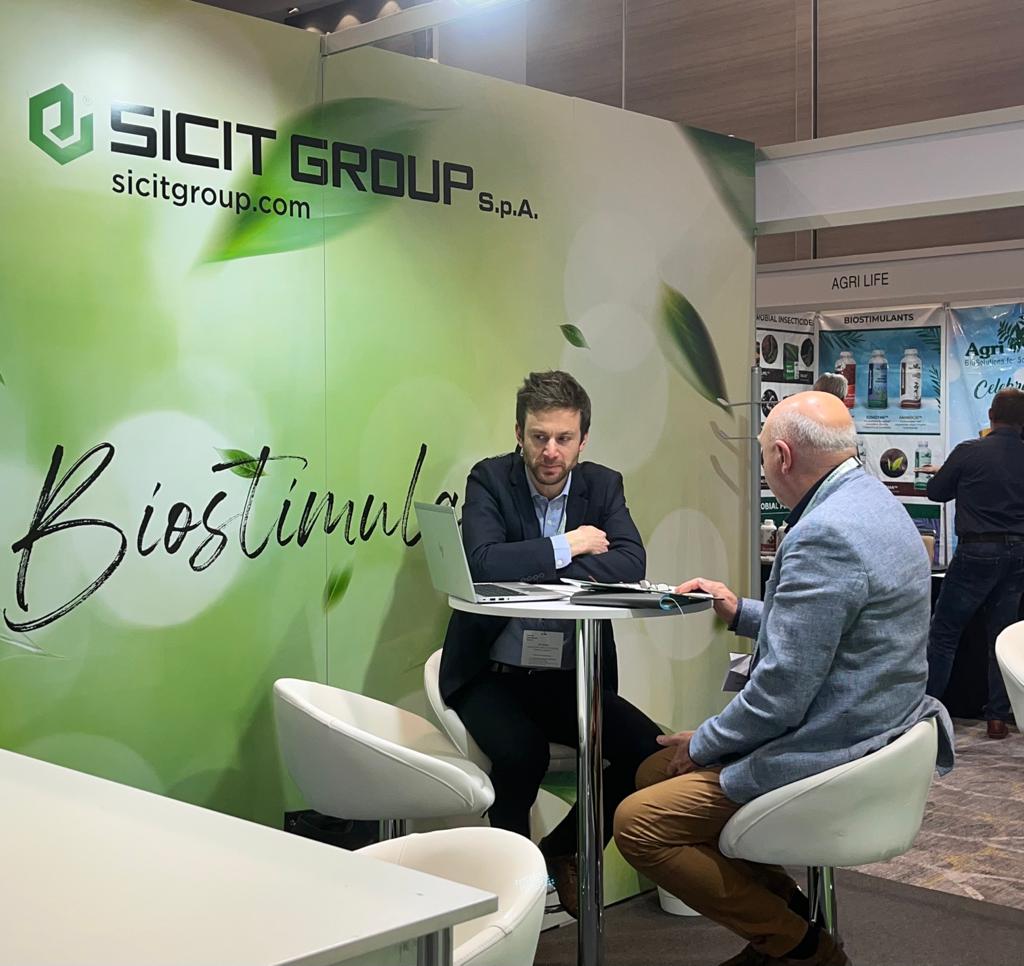 Two professionals discussing BioAg solutions at an exhibitor booth during the New Ag International Annual event in Bangkok.