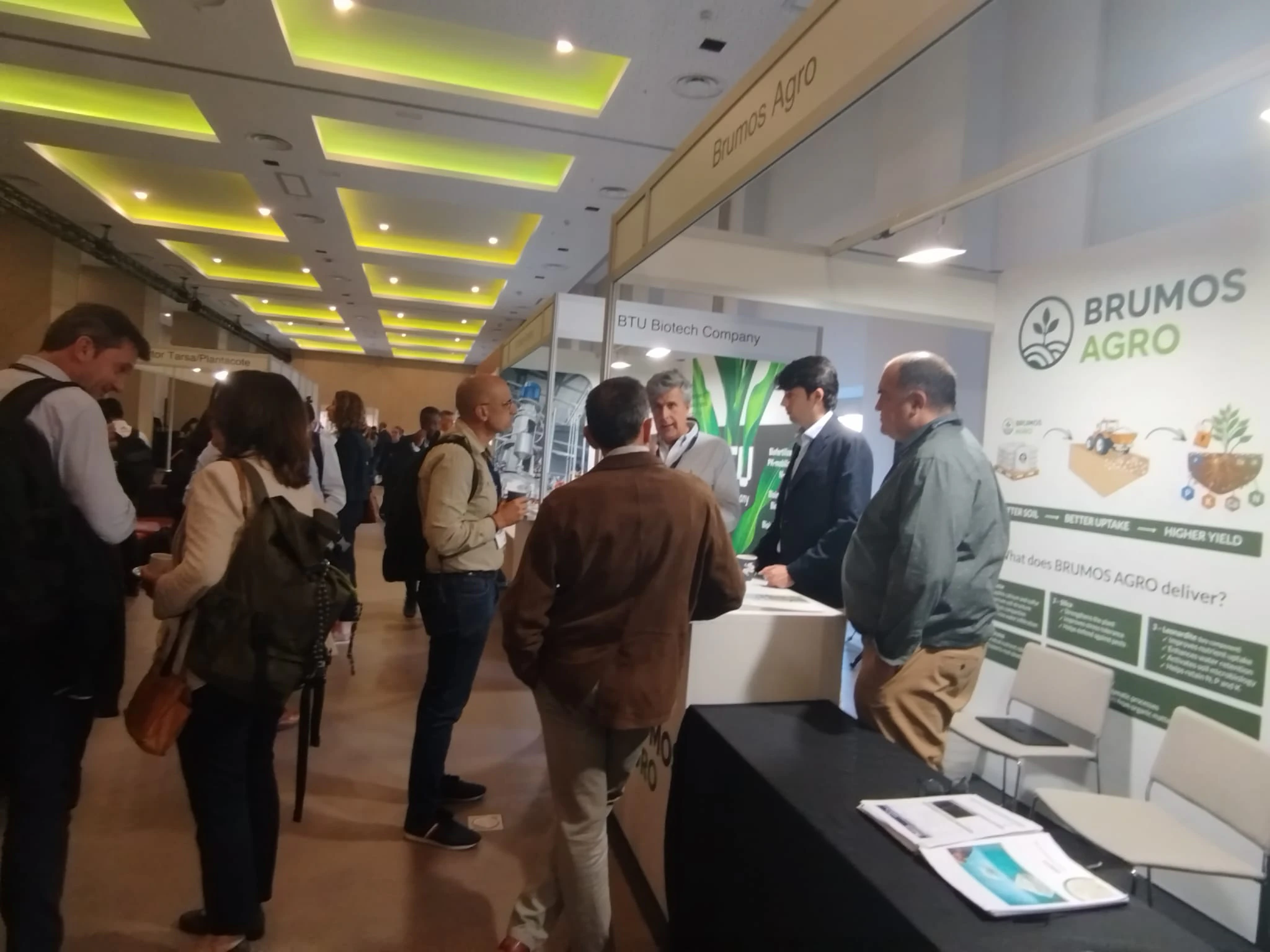 Group of people discussing BioAg solutions at an exhibitor booth during the New Ag International Annual event in Madrid.