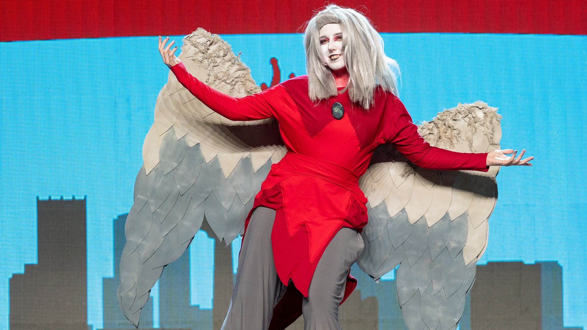 An Eda Clawthorne cosplayer stands onstage with her arms in the air