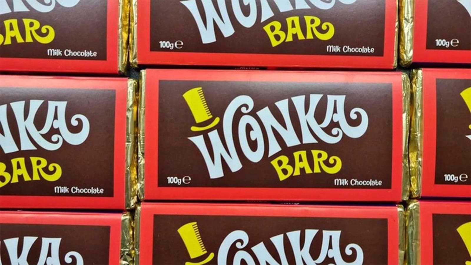 a wall of Wonka bars fills the image box. The chocolate is gold foil wrapped, and the wrapped is brown, with a red boarder, a classic white Wonka logo and a yellow hat.