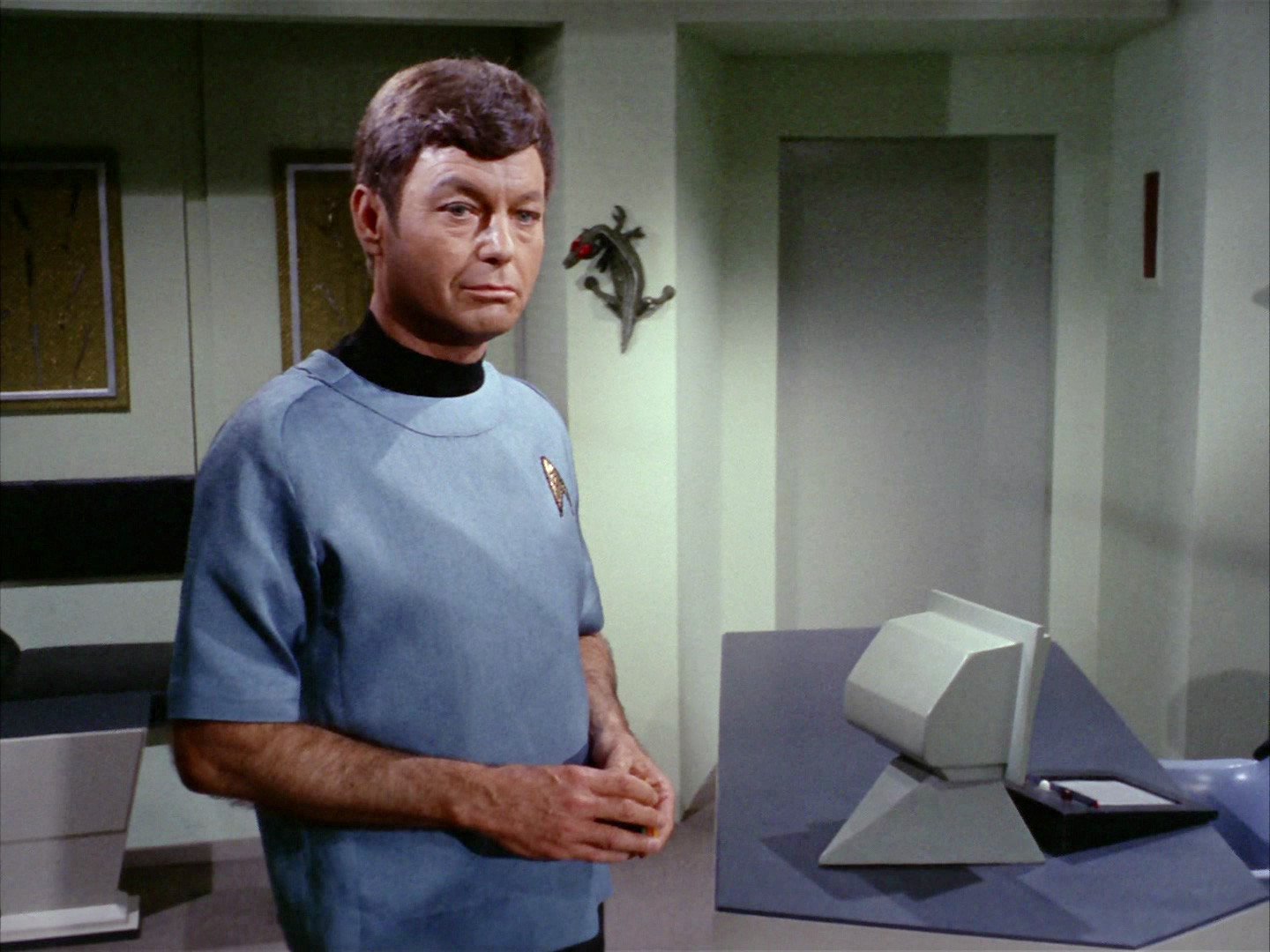 Dr. McCoy stands in the Medical Bay in his Blue enterprise scrubs. The room is varying colours of blues, whites, and greys.