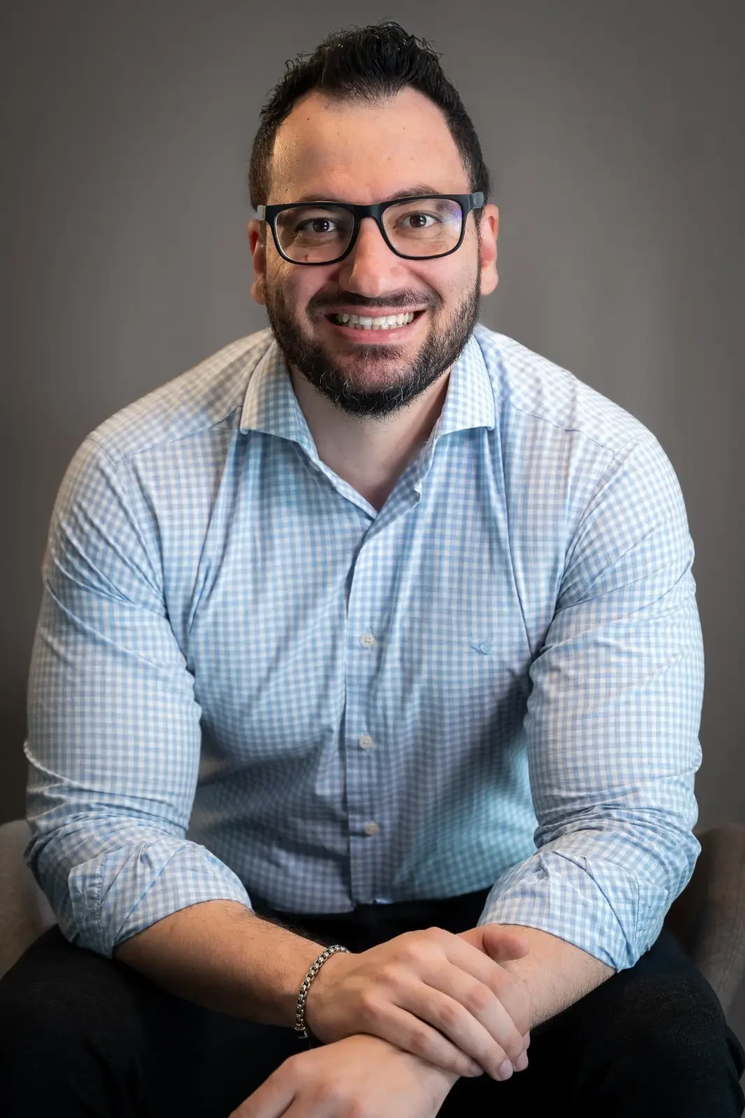 Retrato de Alex Vieira, CIO e VP do HCOR e ABCIS. Um homem jovem de óculos de armação preta, com barba curta e sorriso aberto, vestindo uma camisa social de padronagem xadrez pequena em tons de azul claro e branco.