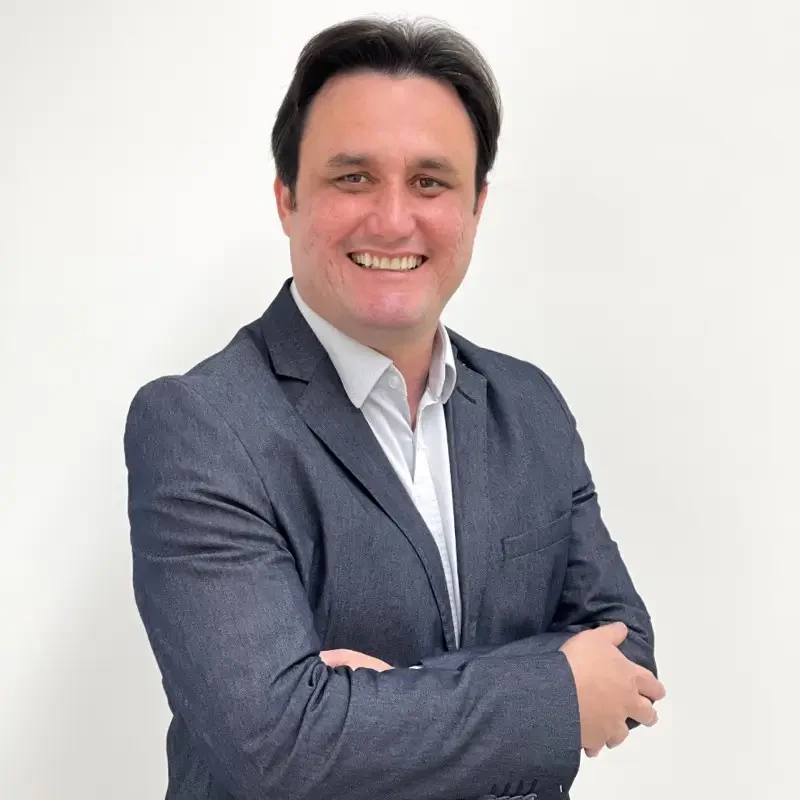 Arthur Alberto Braga Guimarães, palestrante no Healthcare Innovation Show, sorri de braços cruzados usando blazer cinza.