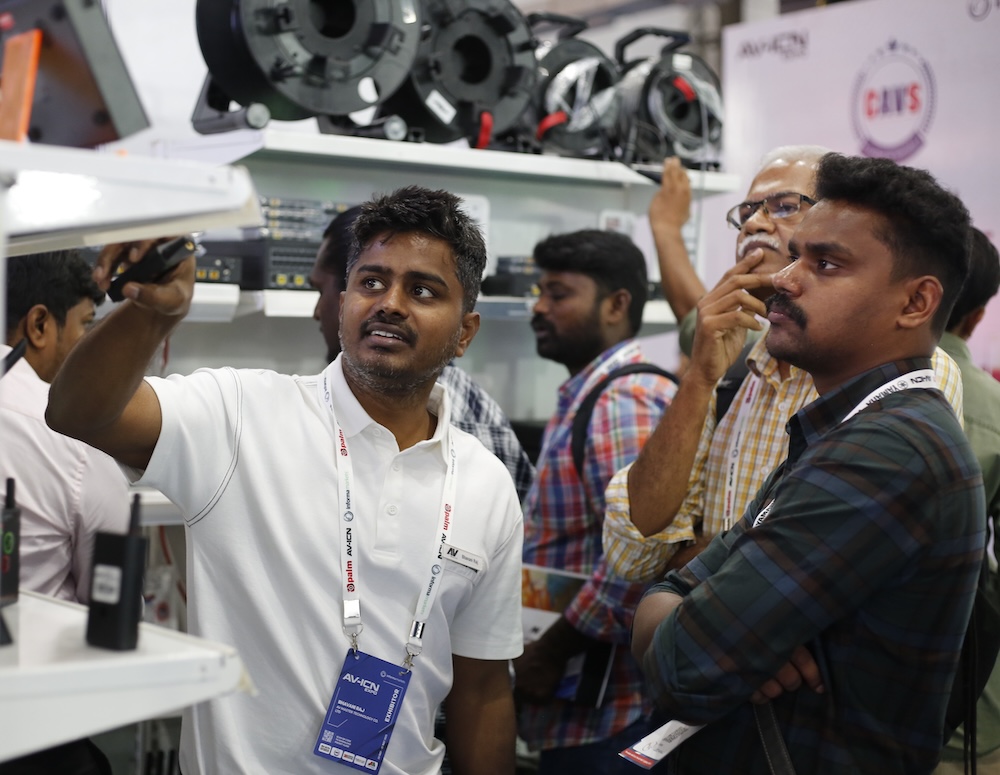 A group of people examining electronic equipment at a technology exhibition or trade show.