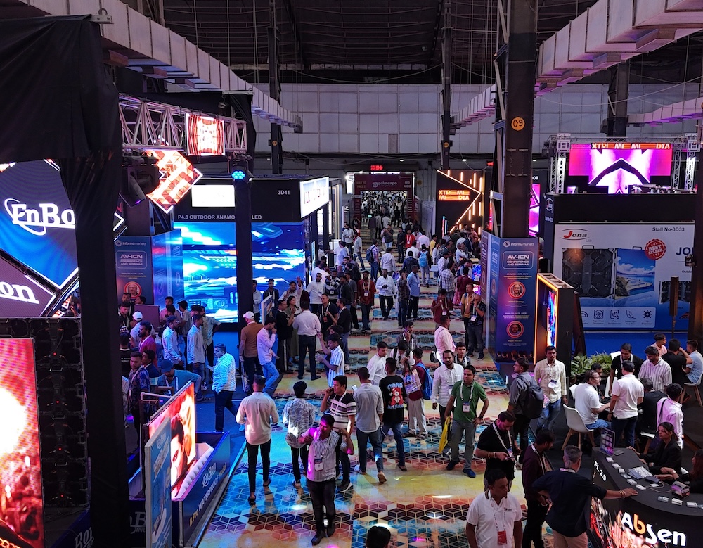 Crowded technology or trade exhibition hall with digital displays and vendor booths.