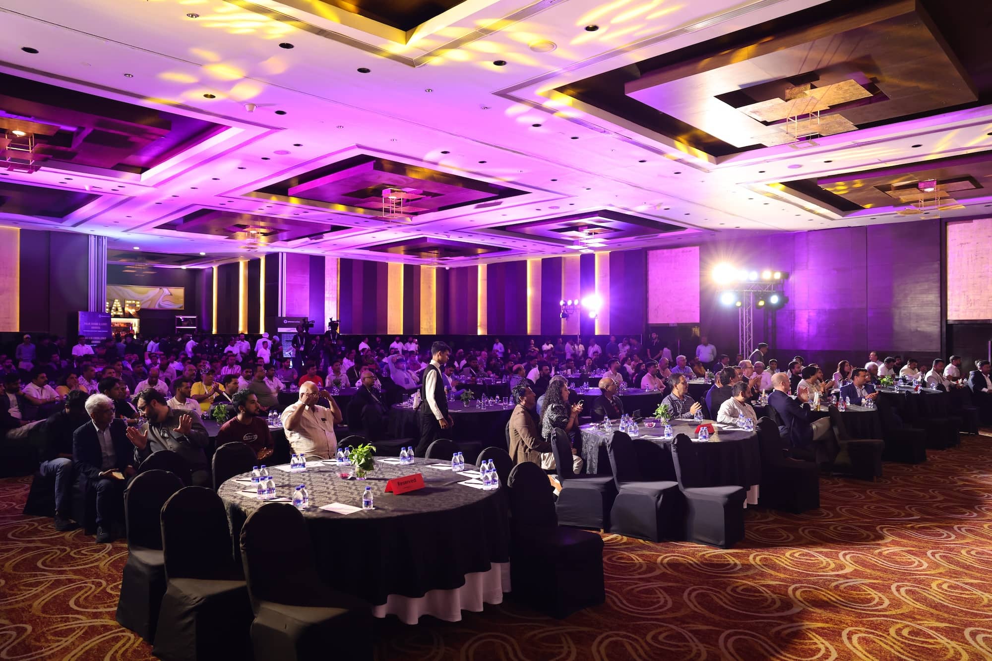 A formal banquet or conference in a ballroom with purple lighting and attendees seated at round tables