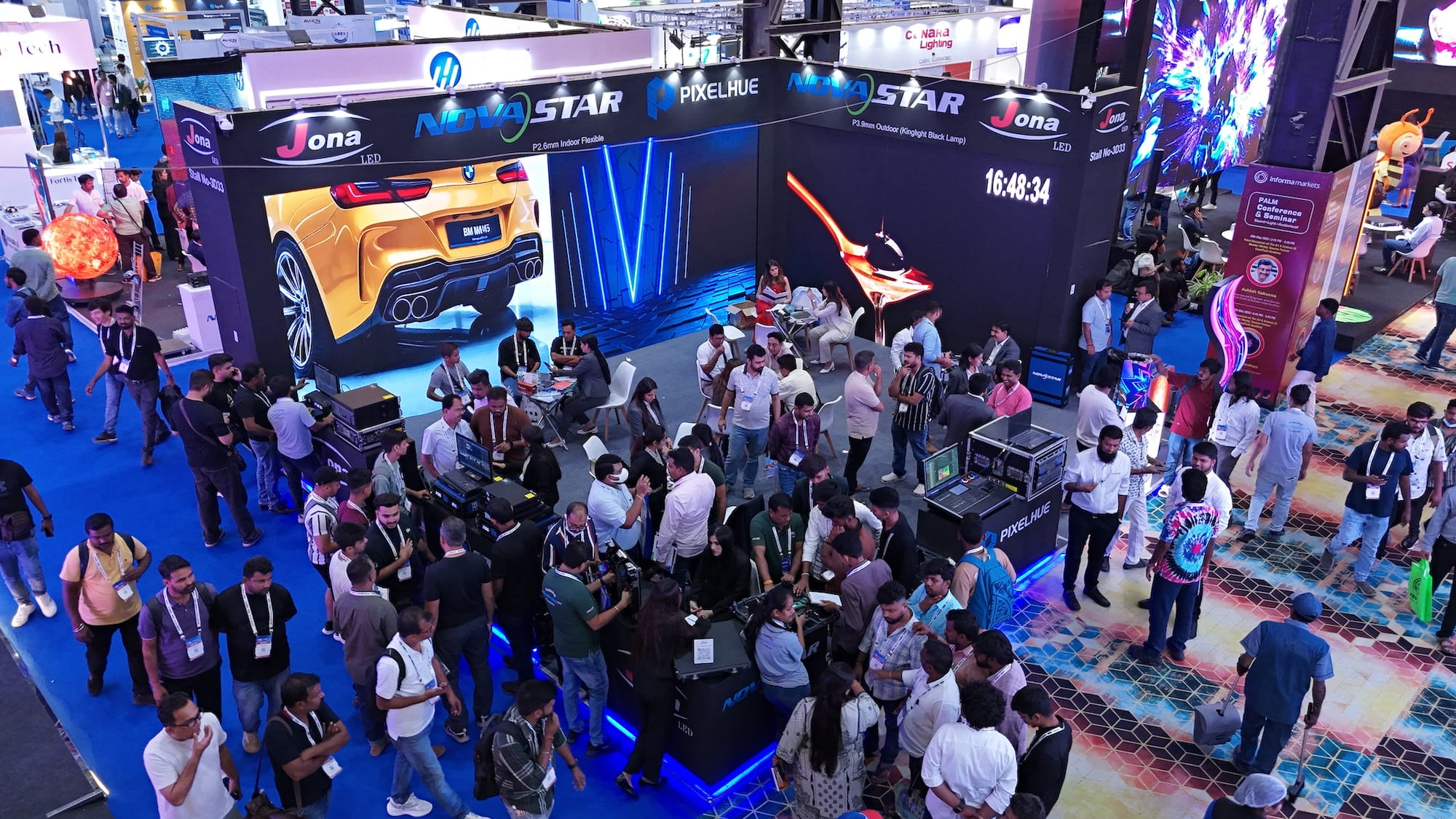 Crowded event technology trade show booth with large screens and an image of a yellow sports car.