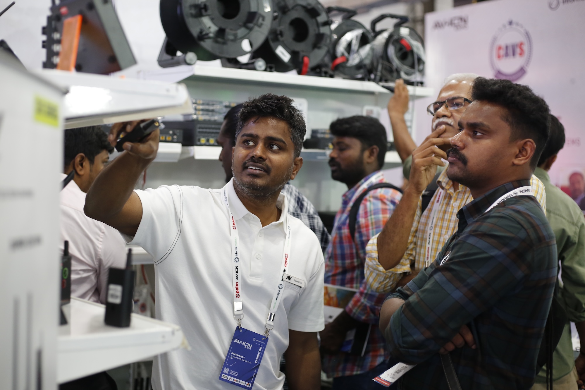A group of people examining electronic equipment at a technology exhibition or trade show.