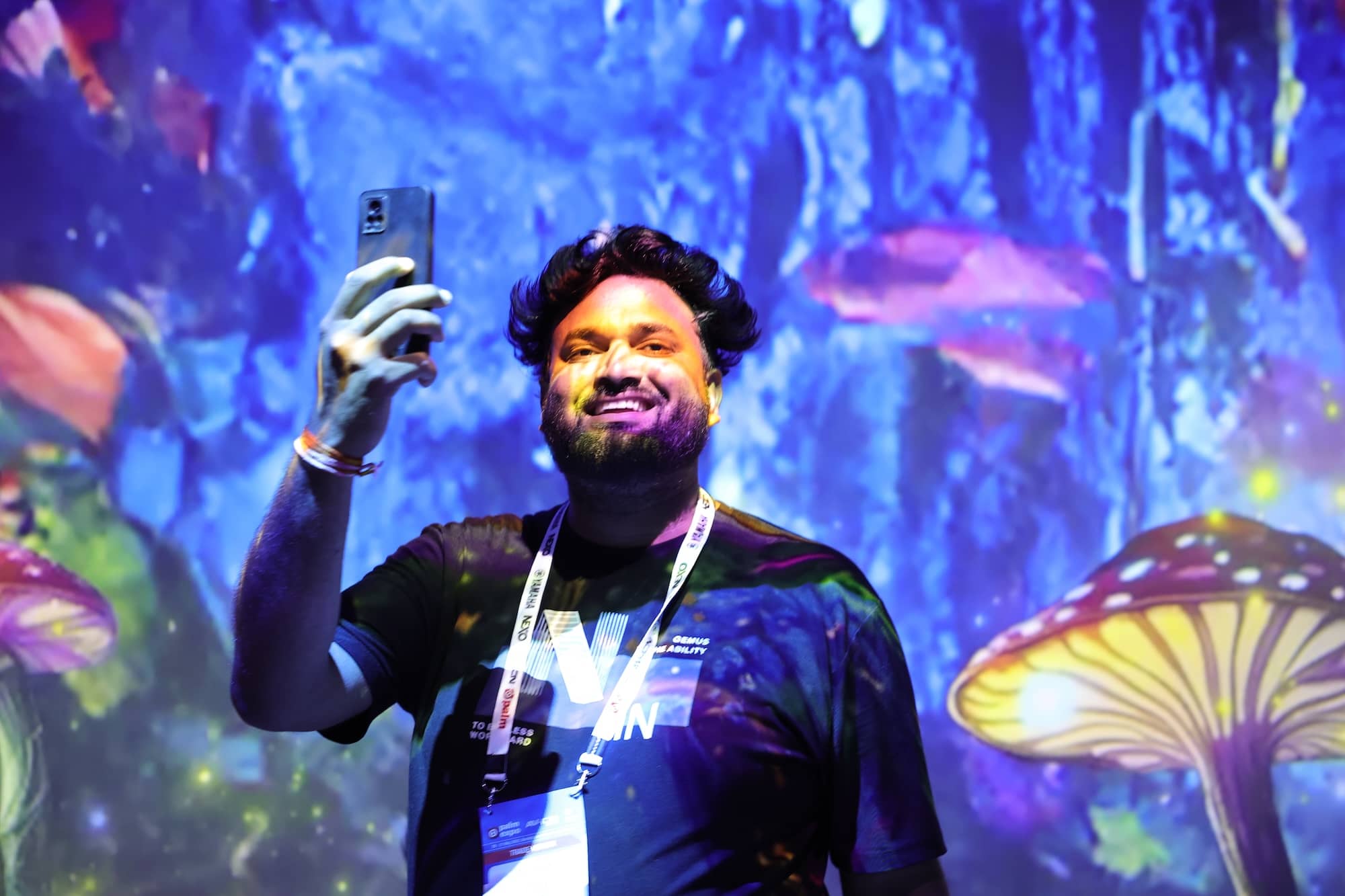 Person taking a selfie at an event with colorful digital mushroom projections in the background.