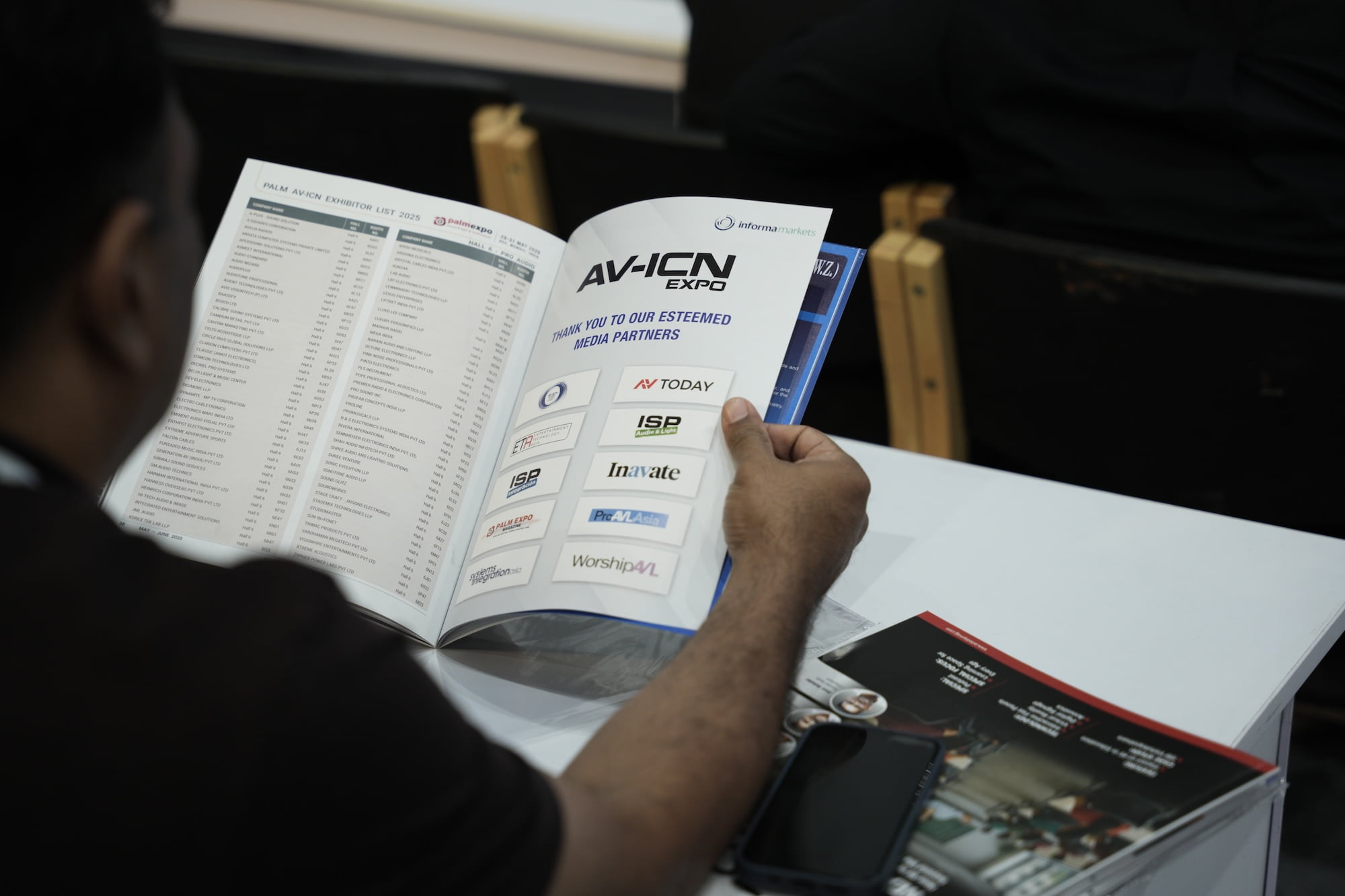 Person reading an AV-ICN Expo program booklet showing media partners page