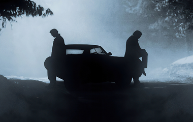 two men leaning against their car at nighttime, under the moonlight