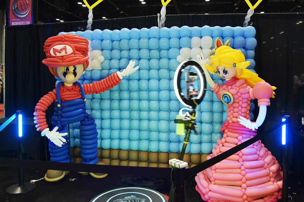 A Mario & Peach balloon sculpture stands next to a balloon wall