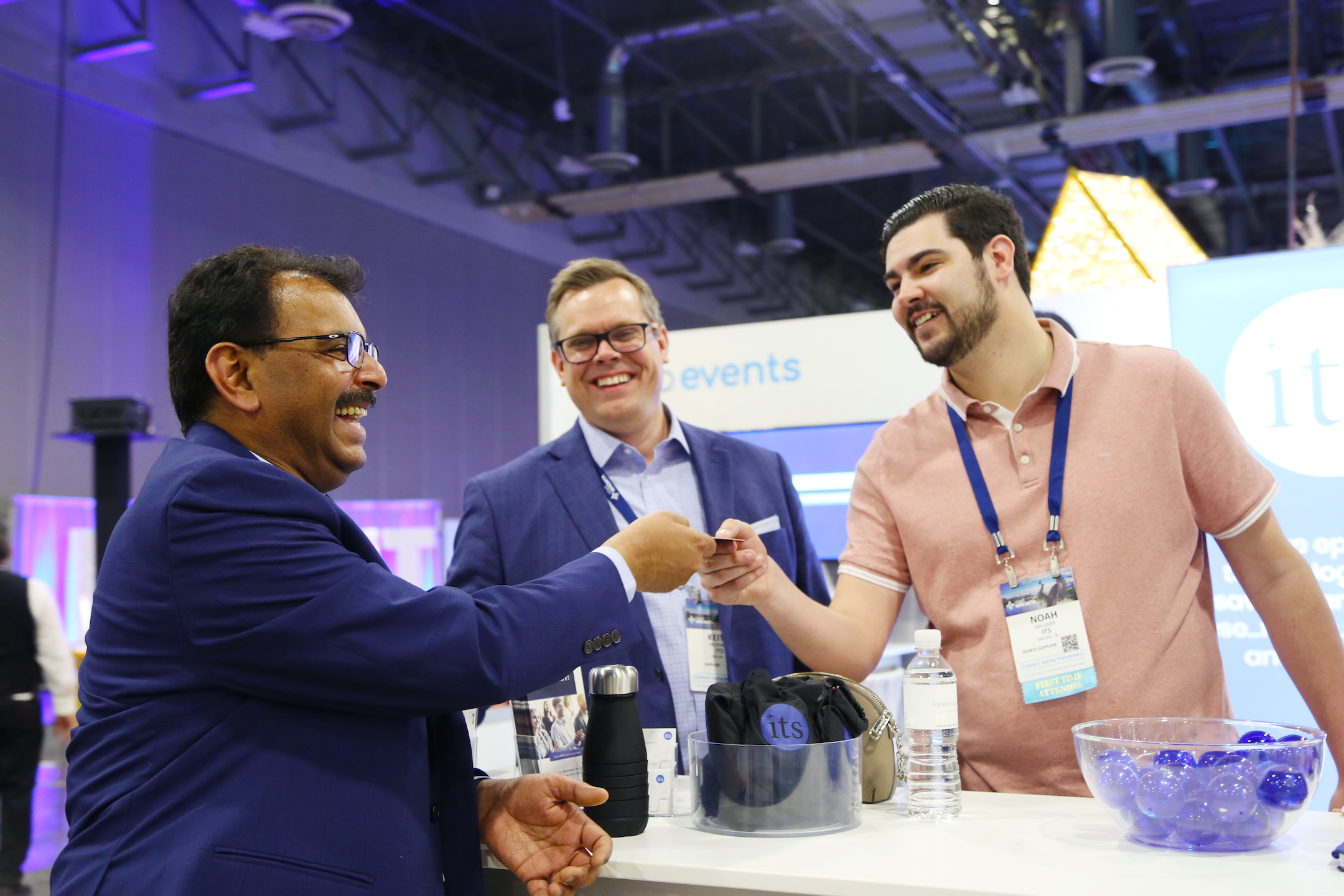 3 men smiling and exchanging business cards at a trade show booth