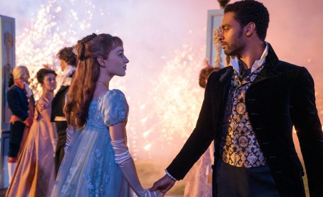 A man in a black tuxedo stands as a woman in a blue dress takes his hand