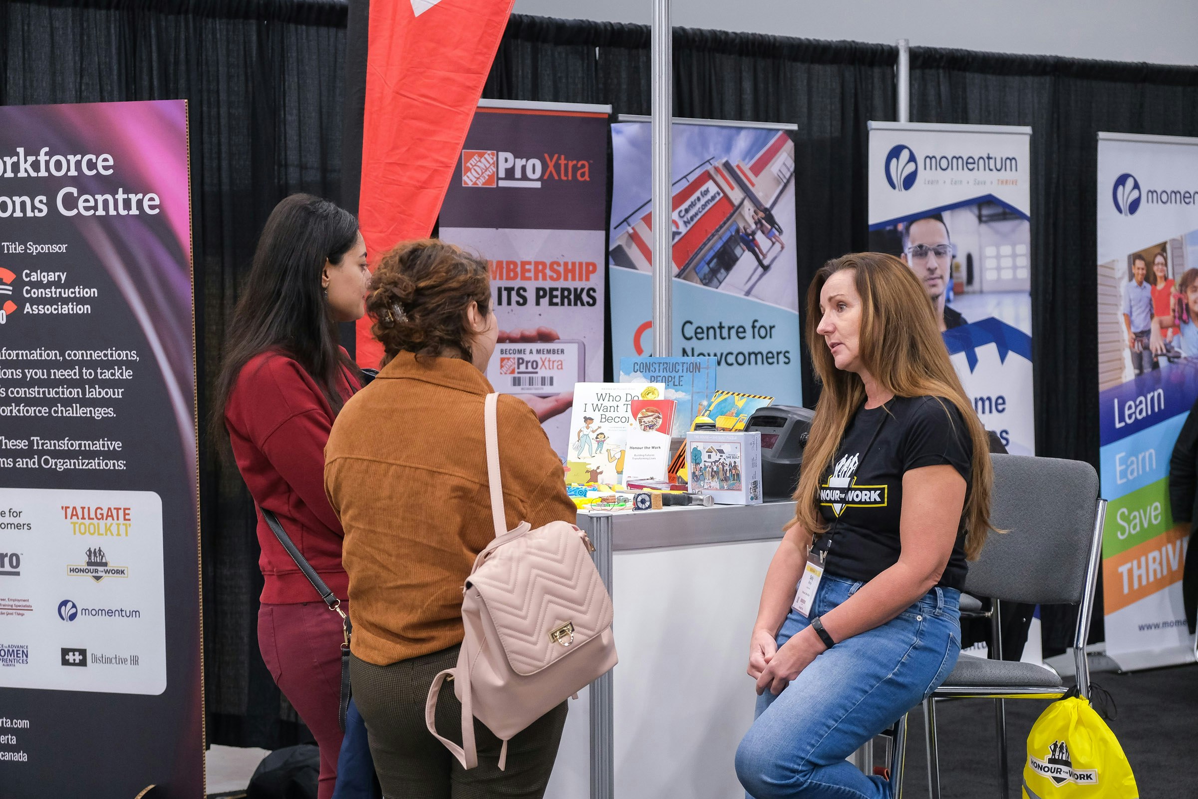 A close up conversation between three attendees at a kiosk in the Workforce Solutions Centre at BUILDEX Alberta.