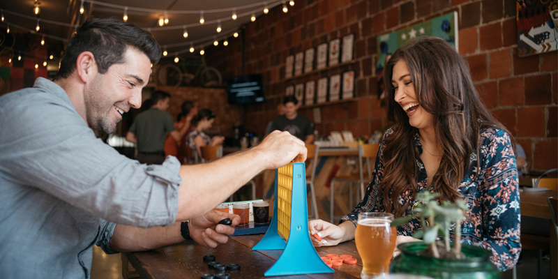 A man and a woman at a brewery in Frsico, TX playing Connect Four.