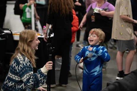 Mother and son play in the Pop Culture Classroom Kids' Lab. With his face painted like Spider-Man, he holds the microphone and laughs with pure joy